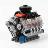 Plastic V8 engine model kit displays black chains, gray pulleys, a front fan, and clear cylinder covers against a white background.