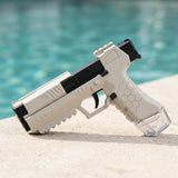 White and black water squirt gun with a hexagonal grip and clear reservoir rests diagonally on a sunlit poolside ledge.