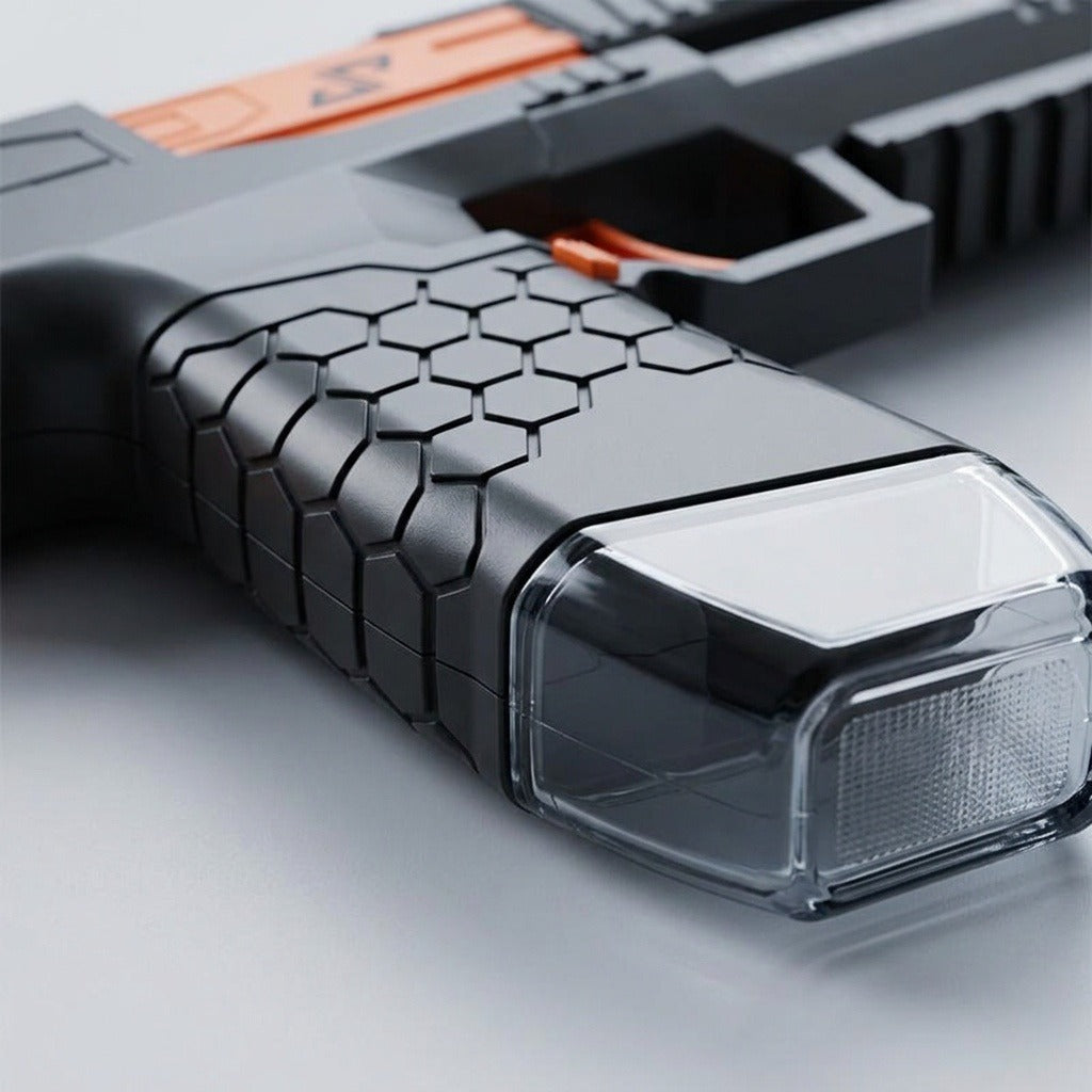 Close-up of a black water squirt gun showing its hexagonal grip texture, orange trigger, and transparent reservoir on a pale surface.