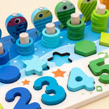 Wooden activity board close-up showing blue and green fish, stacked counting rings, number pieces, and a loose turquoise star.