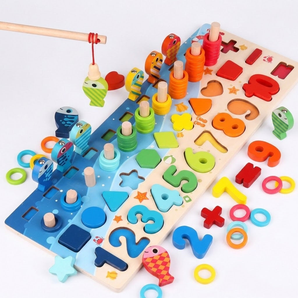 A rod lifts a green fish above a wooden activity board, with loose colorful rings, numbers, and shapes scattered around.
