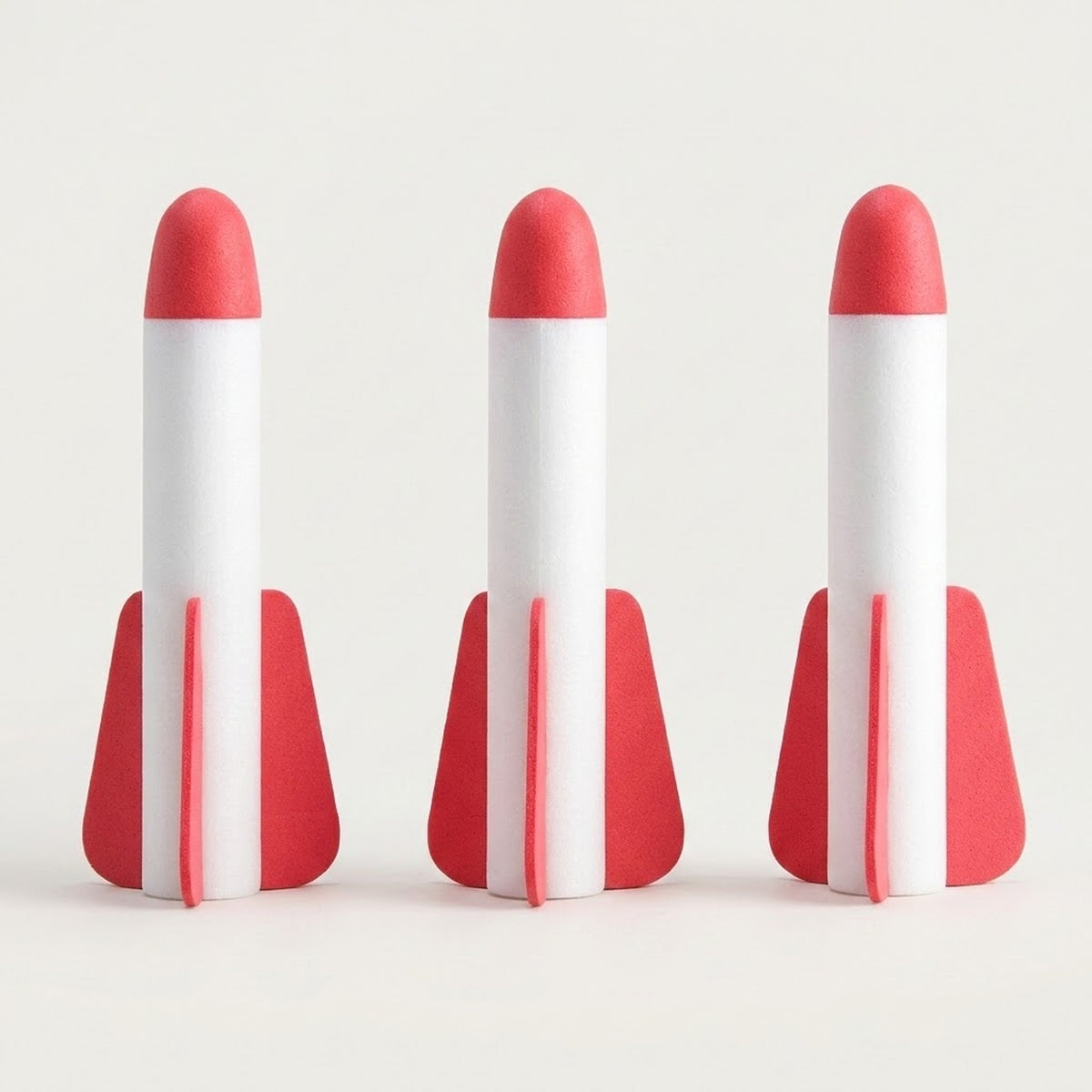 Three white EVA foam rockets with red tips and red fins from a rocket launcher toy standing side by side on an off-white background.