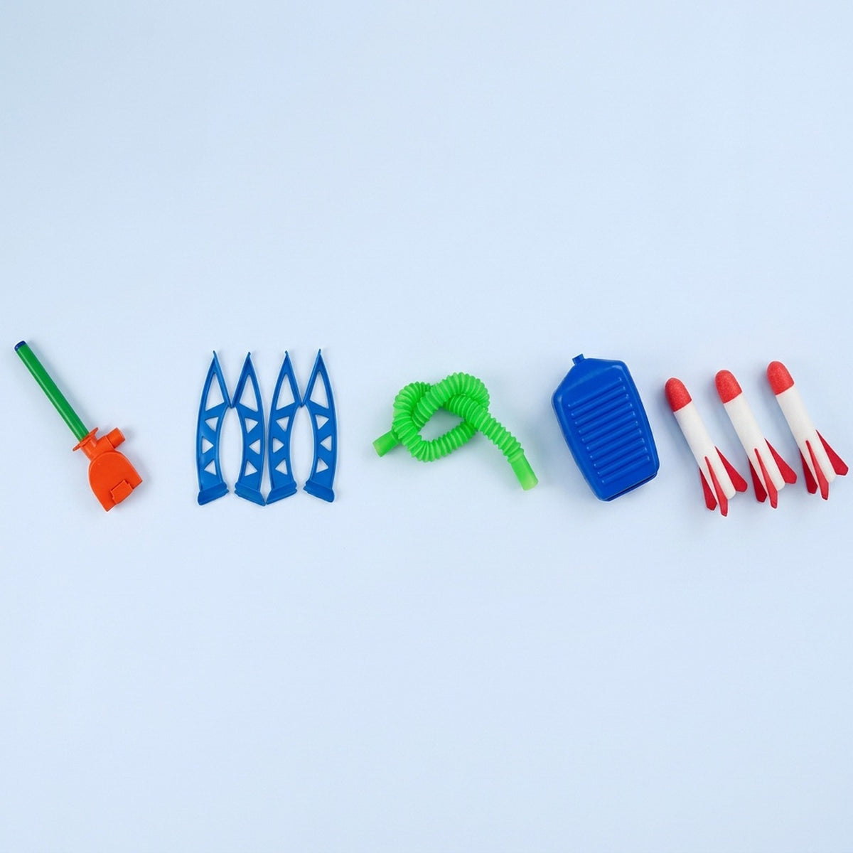 Disassembled launcher-and-3-rockets set of a rocket launcher toy laid out on a pale background, including blue legs, green hose, blue pump, and three red-and-white foam rockets.