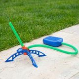 Kids' rocket launcher toy with green launch tube, blue adjustable-angle base and blue foot pump sitting on paving beside green grass.