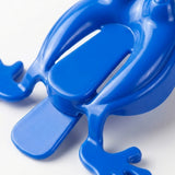 A close-up of a glossy blue plastic jumping frog toy shows its rear pressing tab and molded legs against white.