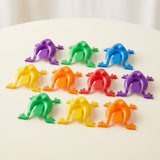 Ten colorful plastic jumping frog toys sit in three rows on a cream tabletop with their rear pressing tabs visible.