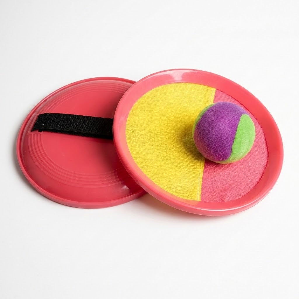 A catch game set displays two pink paddles, a yellow-and-pink cloth face, black strap, and purple-and-green ball against a white background.