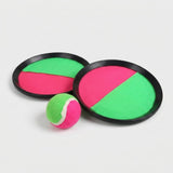 Catch game set with two black-rimmed paddles featuring pink and green cloth faces, with a matching ball in front on light gray.