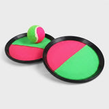 Catch game set with two black-rimmed pink and green paddles and a matching ball resting on the rear paddle against light gray.