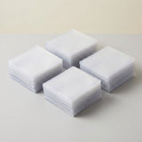 Four neat stacks of translucent plastic card sleeves rest on a light gray tabletop against a cream background.