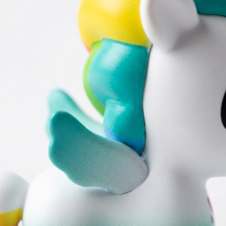 A close-up of the blind box figure shows its turquoise wing, white body and multicoloured mane against white.
