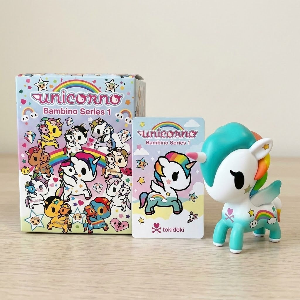 A white and turquoise blind box figure stands beside one illustrated box and one accompanying card on a wooden desktop.