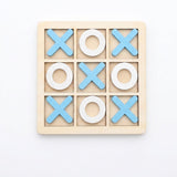 A wooden 3x3 tic-tac-toe game board with light blue X shapes and white O shapes, photographed from above on a plain white background.