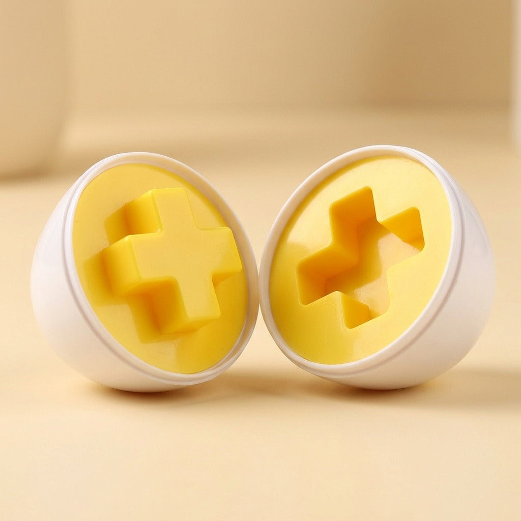 Matching egg set detail showing two white shell halves with yellow raised and recessed cross shapes on a cream surface.
