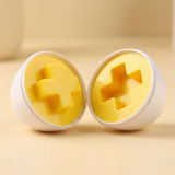 Matching egg set detail showing two white shell halves with yellow raised and recessed cross shapes on a cream surface.