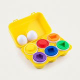 A children's shape-sorting toy set in a bright yellow plastic egg carton case, shown open on a clean white background. The set includes white egg-shaped pieces and six colored circular pieces in yellow, orange, red, green, blue, and purple, each with a matching geometric hole.