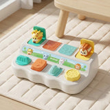 Pop-up toy with giraffe and lion figures raised on a white base with colorful buttons, on a cream quilted rug by a wooden table.
