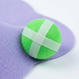 Close-up of a green ball with pale fastening strips resting against the lavender fabric surface of the sticky ball target.