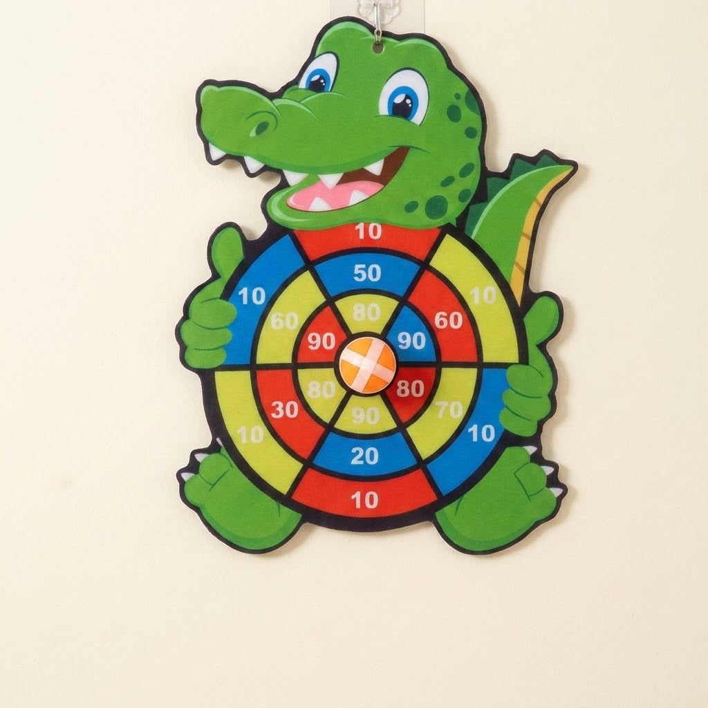 Green crocodile sticky ball target hangs on a cream wall with an orange ball attached to its colorful numbered center.