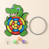 Green crocodile sticky ball target lies on a cream background beside a gray hoop, three colorful balls, and an adhesive hook.