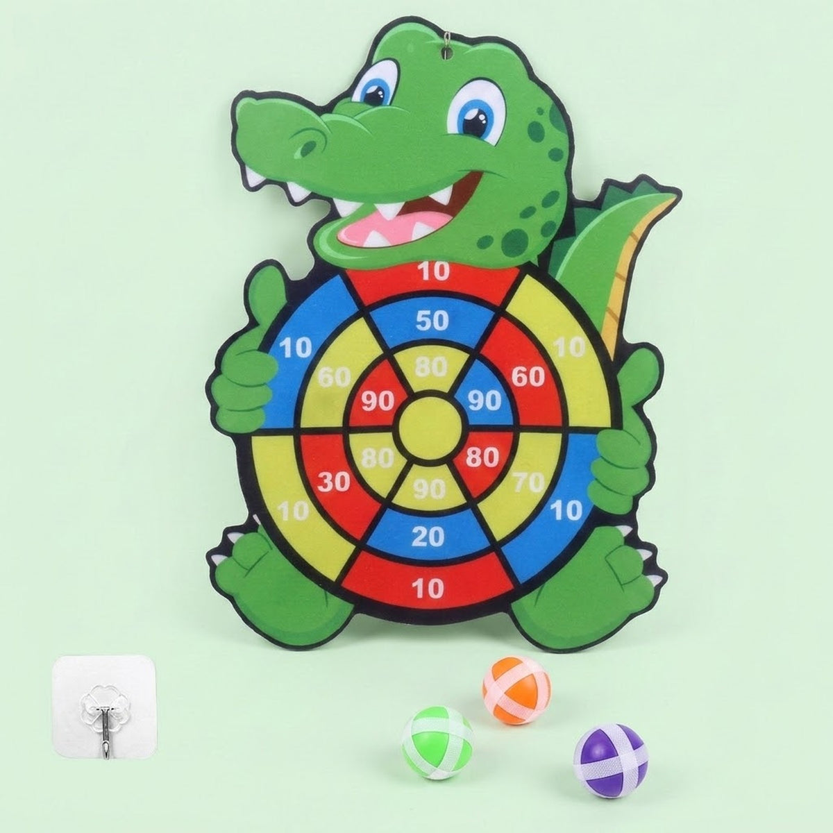 Green crocodile sticky ball target with red, blue, and yellow scoring sections appears beside three balls and a hook against pale green.