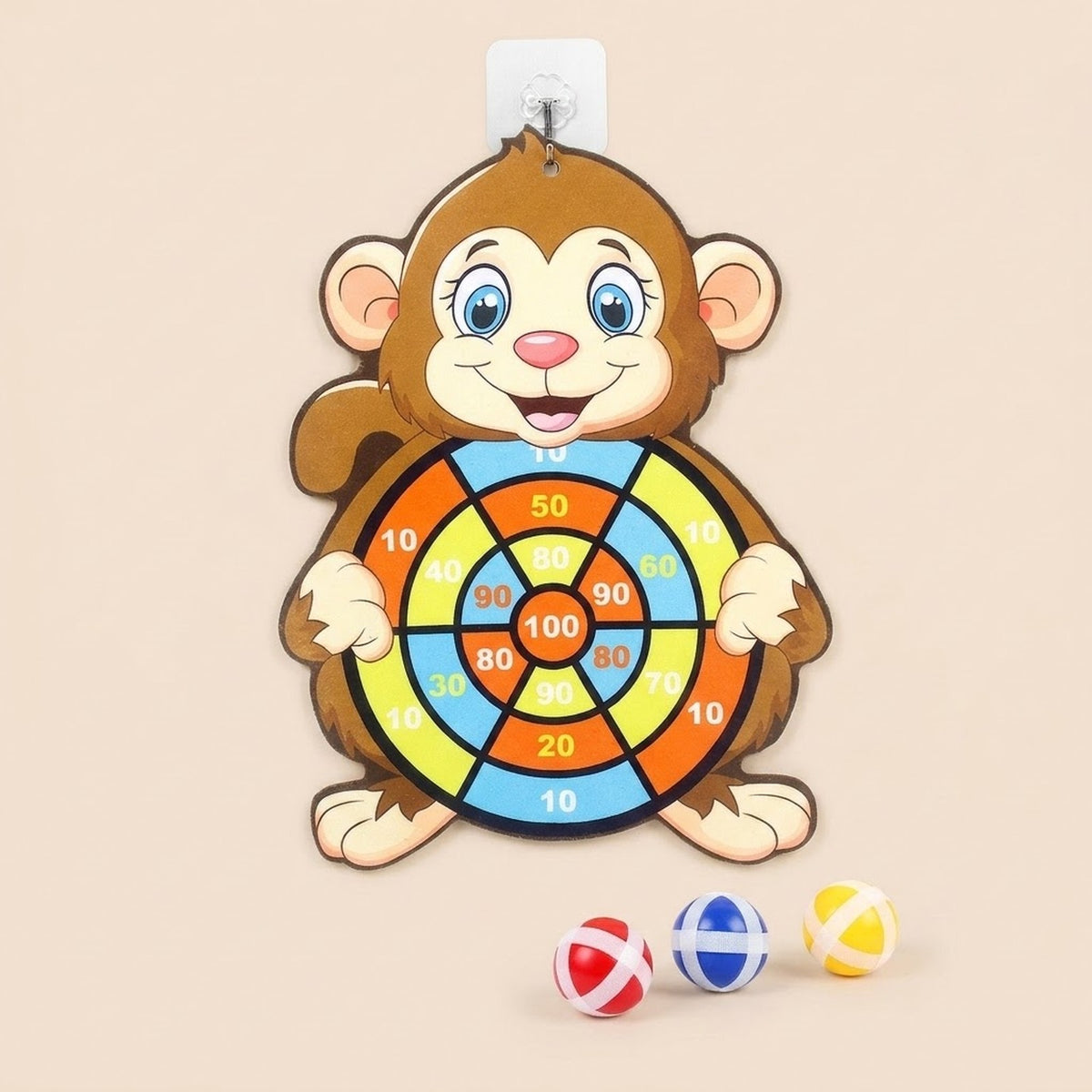 Brown monkey sticky ball target hangs against a beige background above red, blue, and yellow balls, with its adhesive hook visible.
