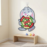 Gray rabbit sticky ball target hanging on a beige wall above a wooden bench holding blue, yellow, and red balls.