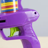 Close-up of a purple plastic disc shooter shows its textured grip, green trigger, and colorful discs against a pale gray background.