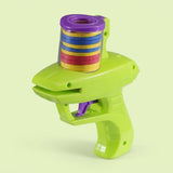 A lime green plastic disc shooter with purple accents and stacked yellow, blue, and red discs stands against a pale green background.