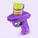 A purple plastic disc shooter with lime green accents and stacked yellow, blue, and red discs stands against a pale lavender background.