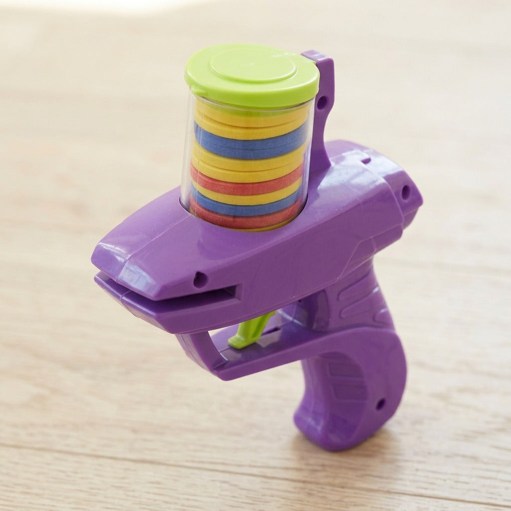 Purple plastic disc shooter viewed from above stands on light wood with colorful discs beneath its closed green lid.