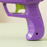 A close-up shows the purple plastic disc shooter's ridged handle and lime green trigger against a cream background.