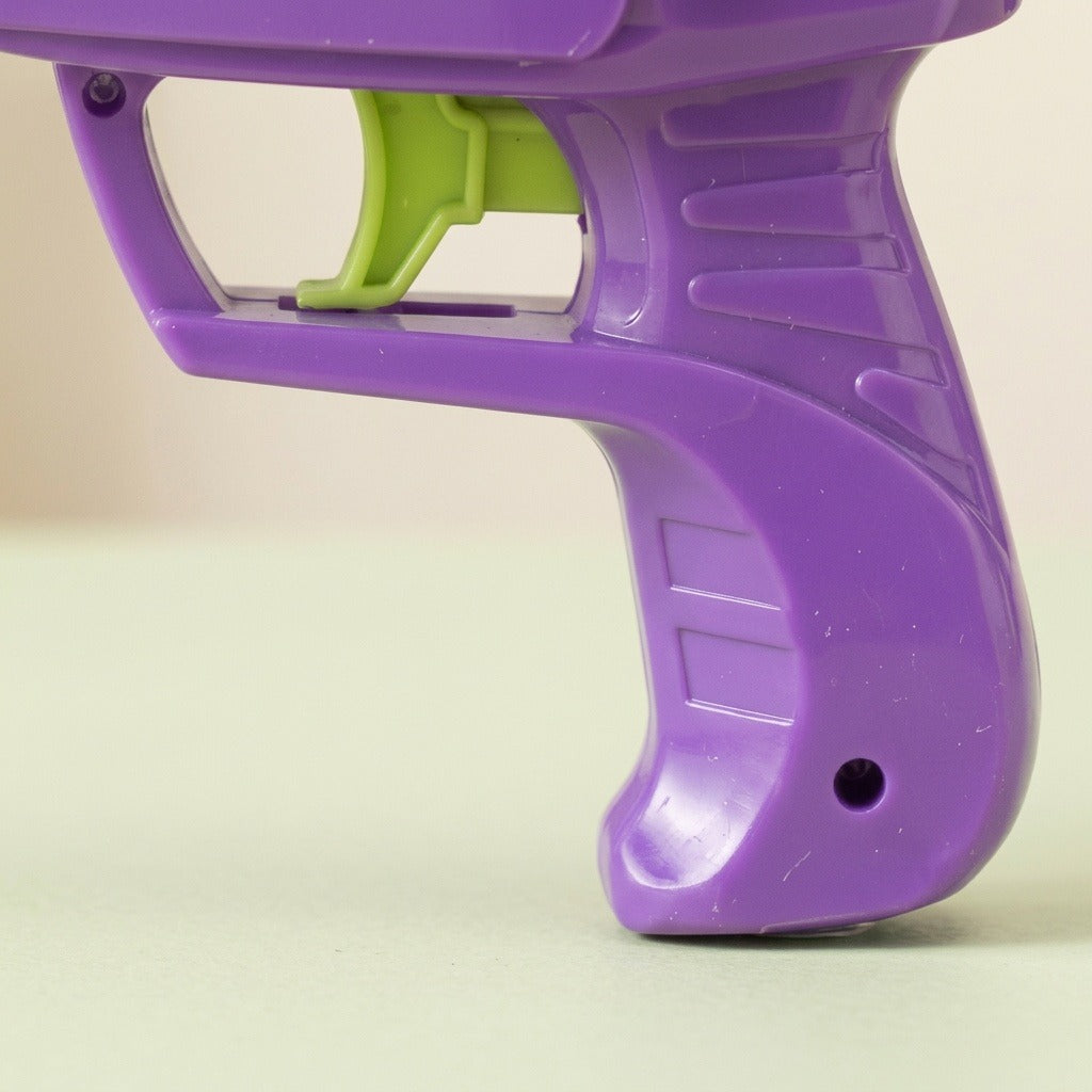 A close-up shows the purple plastic disc shooter's ridged handle and lime green trigger against a cream background.