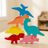 Six colorful wooden dinosaur stacking blocks form a tall balancing tower on a light wooden table in a softly blurred playroom.