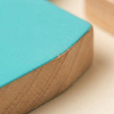 Close-up of one turquoise dinosaur stacking blocks piece shows its colored surface and exposed wooden edge on a pale tabletop.