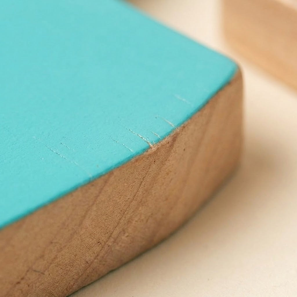 Close-up of one turquoise dinosaur stacking blocks piece shows its colored surface and exposed wooden edge on a pale tabletop.