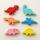 Six wooden dinosaur stacking blocks in red, turquoise, orange, blue, pink, and yellow lie in two columns on a cream background.