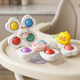 White rabbit, pink pig and yellow duck suction spinner toys with colorful inserts rest on a cream high chair tray.