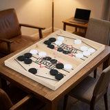 Light wood sling puck game with black and white pucks on a wooden table in a warmly lit room.