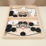 Light wood sling puck game with black and white pucks, elastic cords, and a central divider on a beige surface.