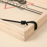 Close-up of the sling puck game showing a knotted black elastic cord around the light wood frame on a beige surface.