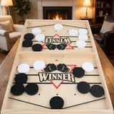 Light wood sling puck game with black and white pucks on a wooden table in a living room with a fireplace.