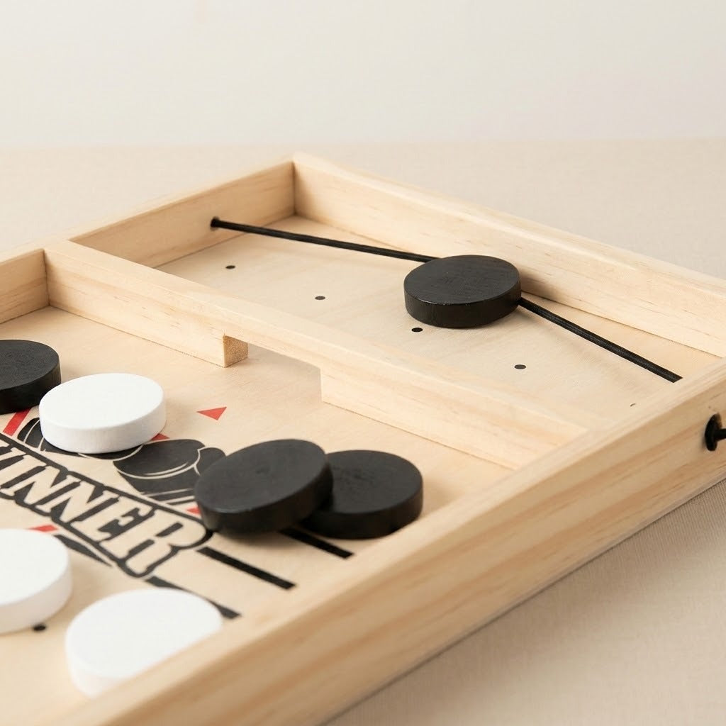 Close-up of a wooden sling puck game showing the central opening, black elastic cord, and black and white pucks against beige.