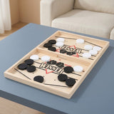 Wooden sling puck game with black and white pucks and elastic ropes on a blue table in front of a cream armchair.