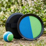 Catch game set with two black plastic discs, a blue-and-green catching face, rear hand strap, and matching ball on grassy ground.