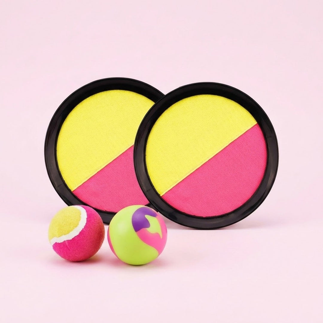 Pink and yellow catch game set includes two black-rimmed discs and two multicoloured balls against a pale pink background.