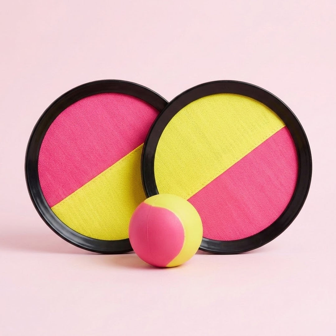 Catch game set with two overlapping pink and yellow discs, black plastic rims, and a matching ball on a pale pink background.