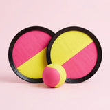 Catch game set with two overlapping pink and yellow discs, black plastic rims, and a matching ball on a pale pink background.