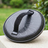 Catch game set disc showing its black plastic back and hook-and-loop hand strap on a stone surface against blurred greenery.
