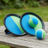 Catch game set with two blue-and-green discs and two balls, one attached to a catching face, on a weathered outdoor table.